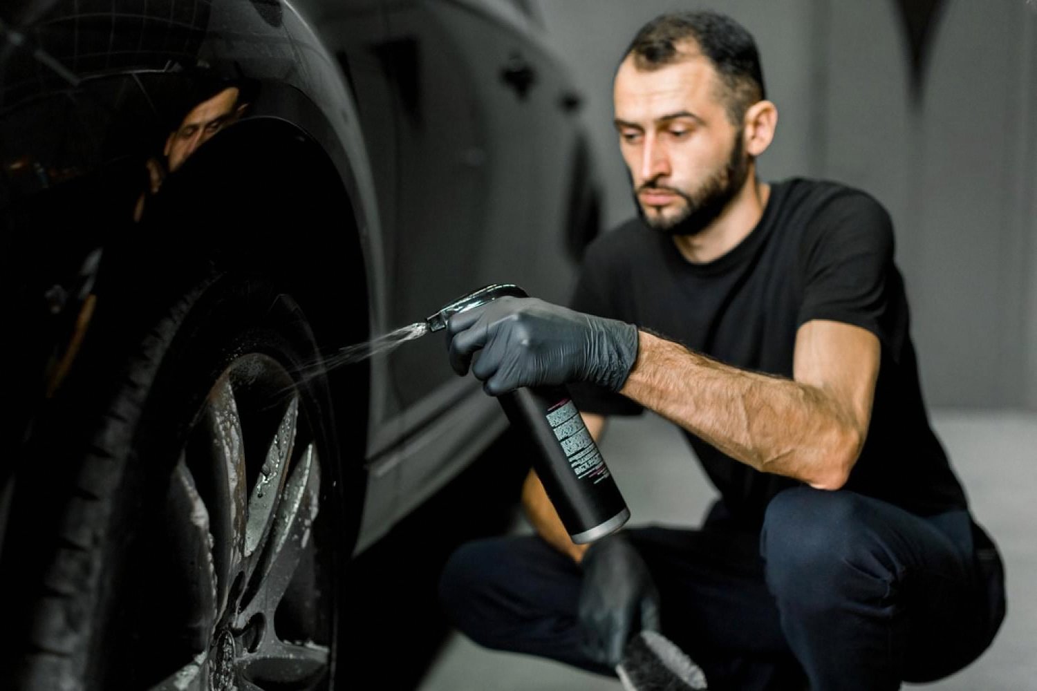 Detailer applying a spray-on ceramic protectant to a car wheel arch in a UAE studio