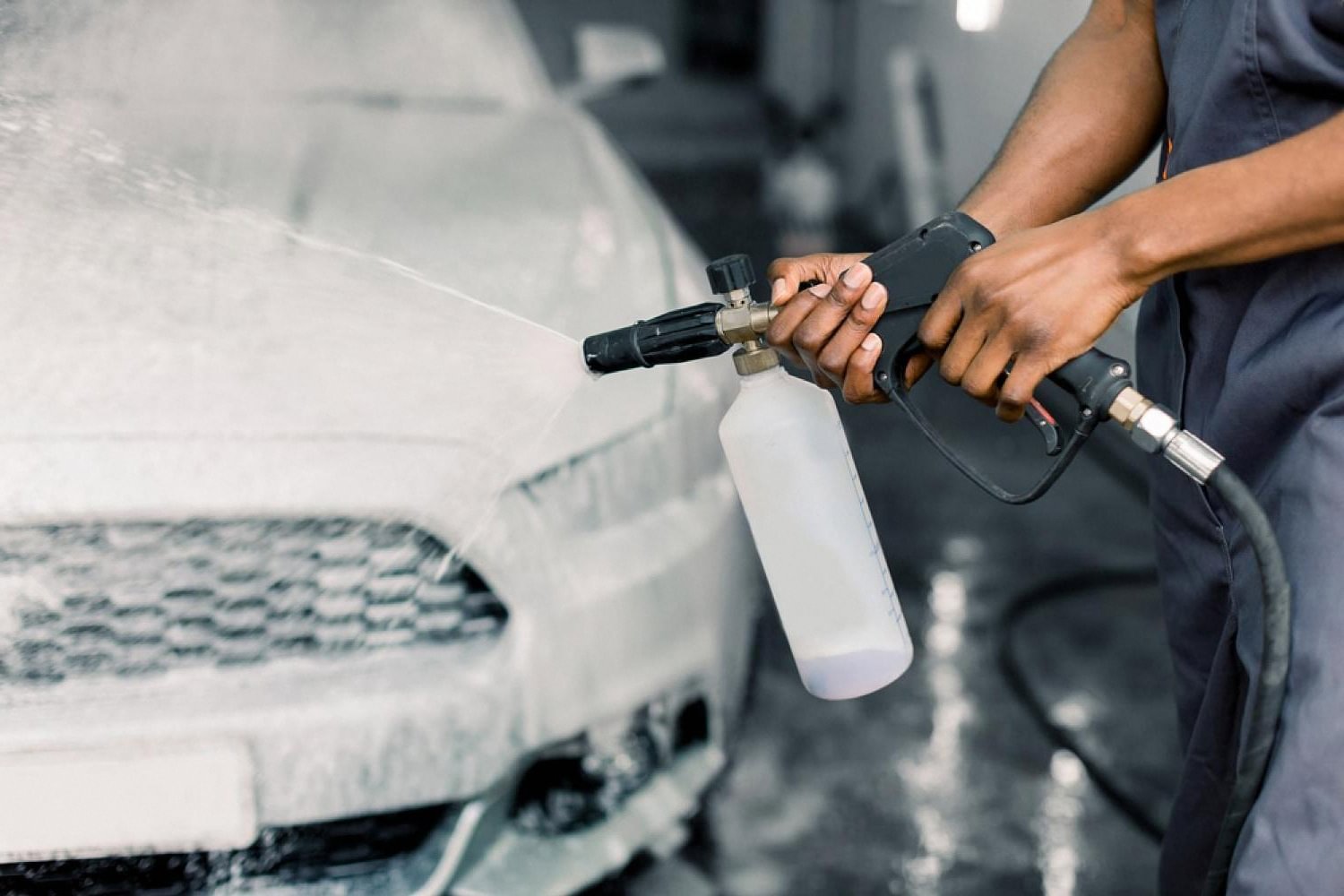 Detailer spraying pH-neutral foam onto a car bonnet during a safe hand wash in the UAE